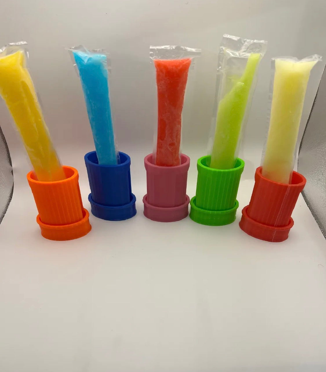 Freeze pop holders in 5 colors — orange, blue, pink, green, red — each holding a freeze pop