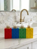 Four building block soap dispenser holders in red, blue, green, and yellow on a kitchen counter