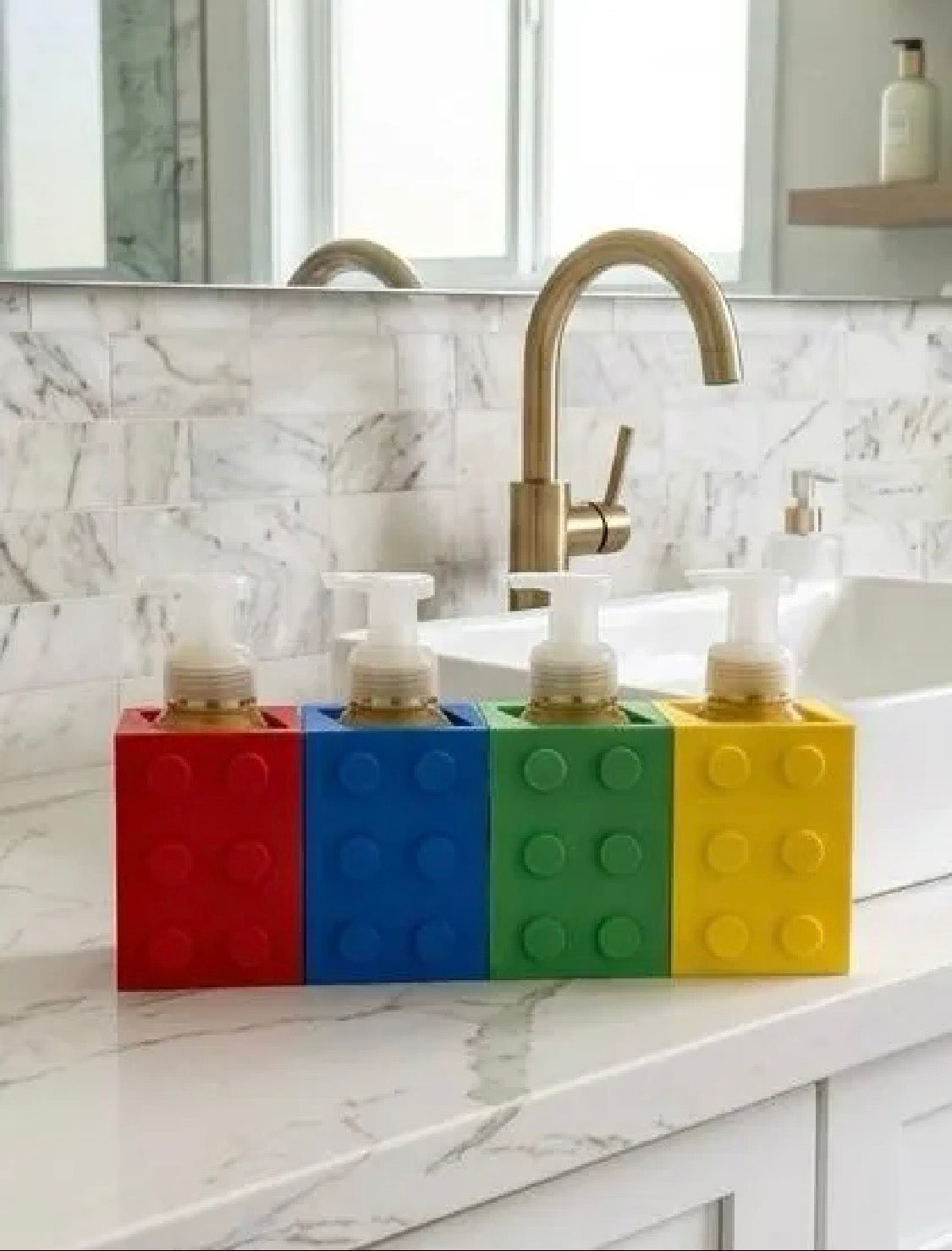 Four building block soap dispenser holders in red, blue, green, and yellow on a kitchen counter