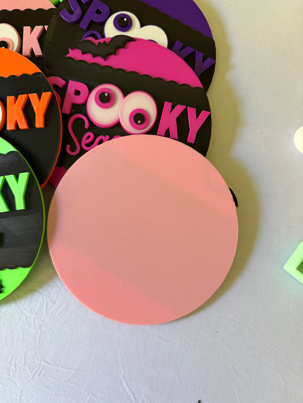 Pink reverse side of a round sign beside colorful Spooky Season Halloween designs