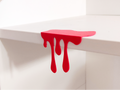 Red 3D printed blood drip decoration clipped onto white shelf edge, front view