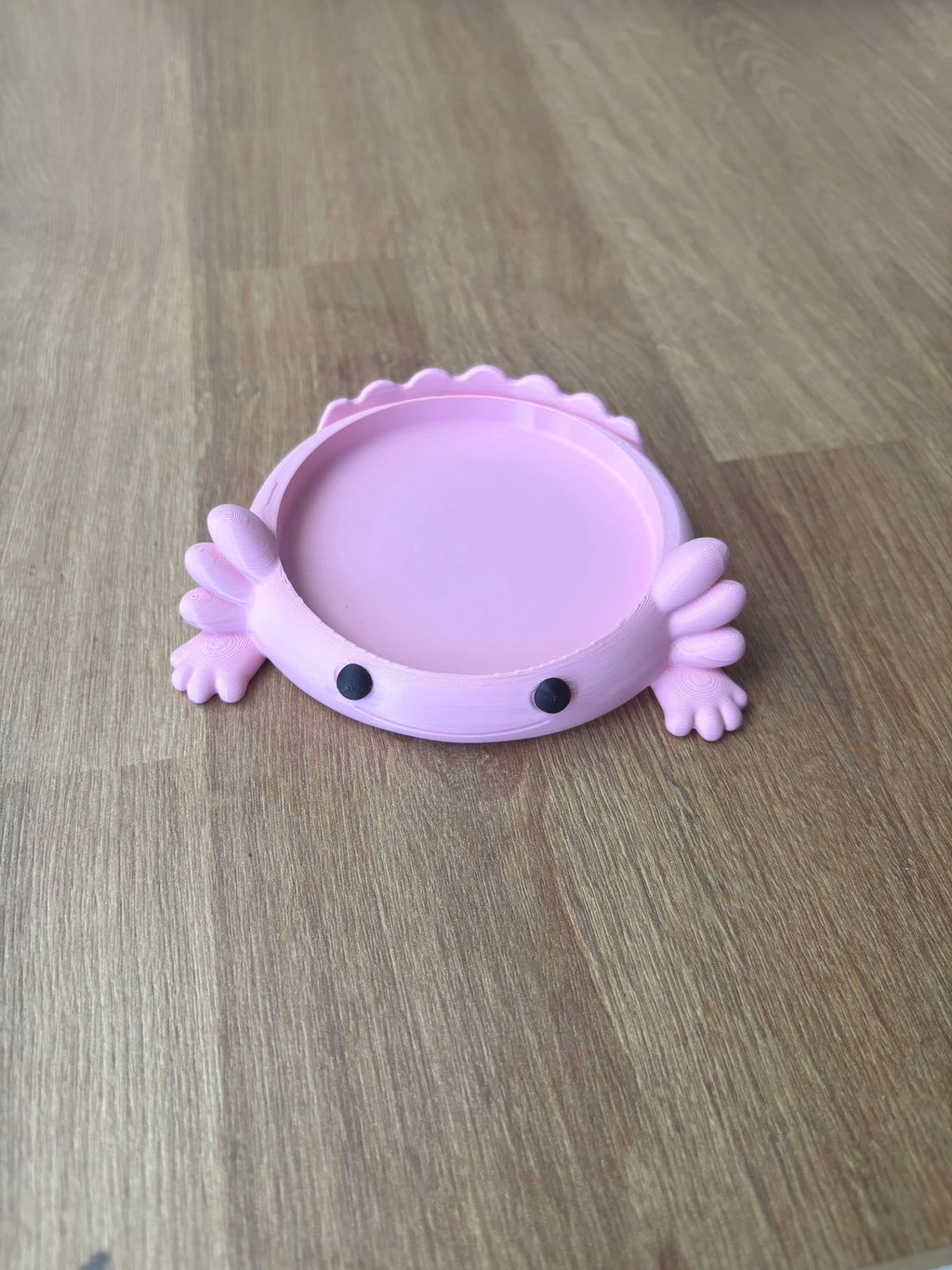 Pink Axolotl coaster holding a white coffee mug on a desk