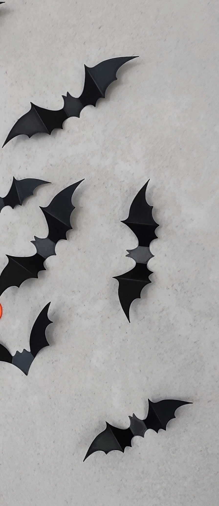 Eight matte black 3D printed bat wall decorations scattered on a grey textured wall