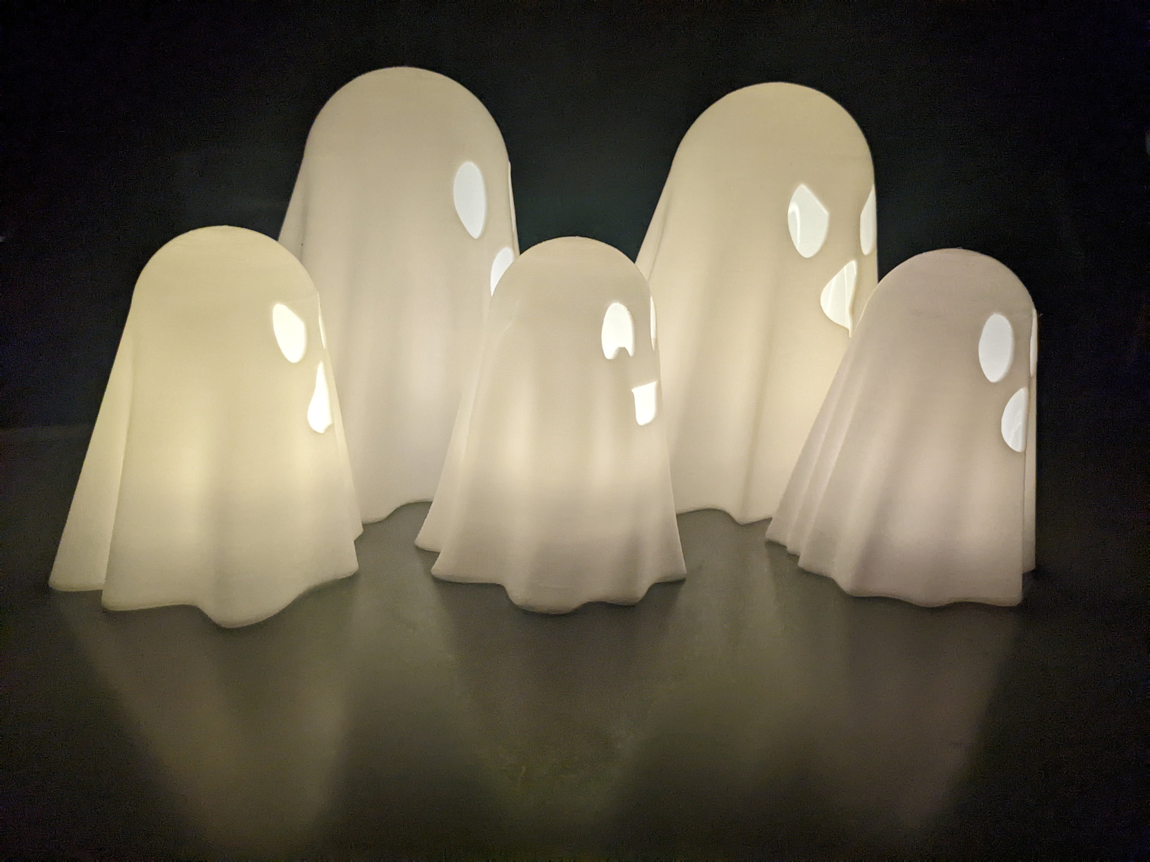 Five 3D printed ghost lanterns glowing warmly in the dark, grouped together