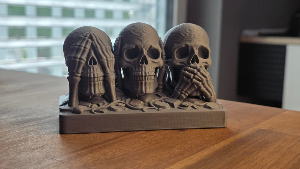 Three see hear speak no evil skulls with skeletal hands, front view on wooden table