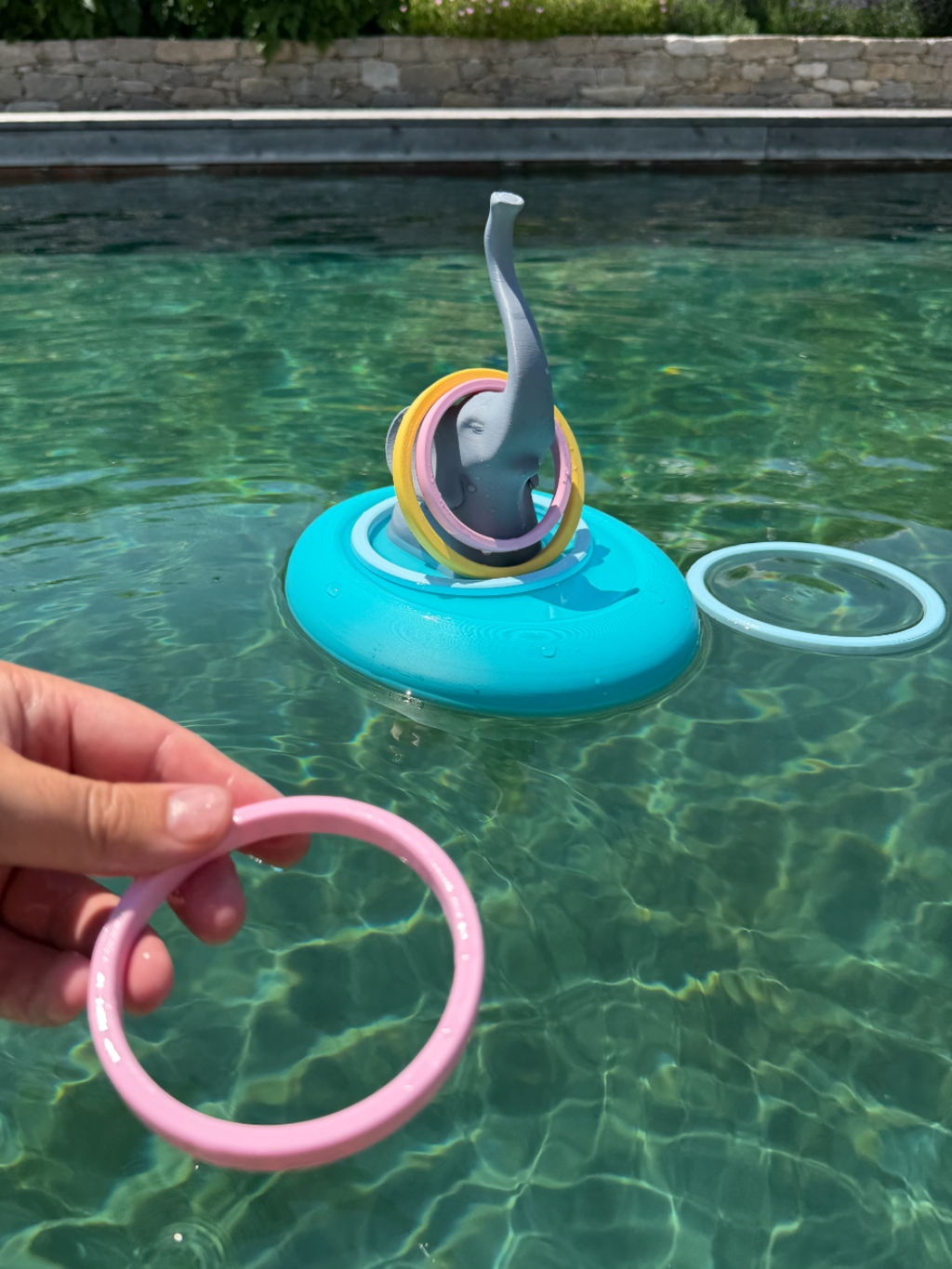 Hand tossing a pink ring toward a floating elephant ring toss game in a pool