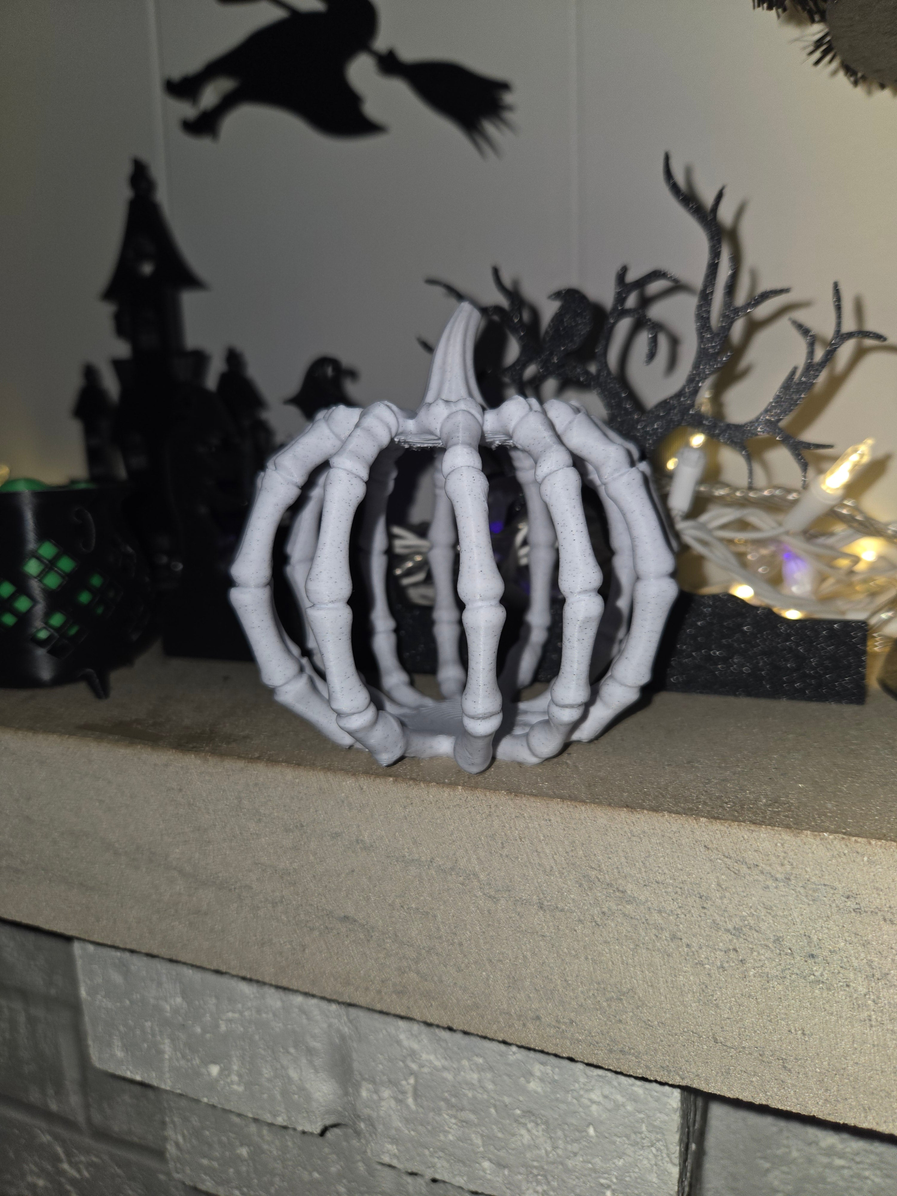 White skeleton hand pumpkin displayed on a stone mantel with Halloween silhouette decor in background