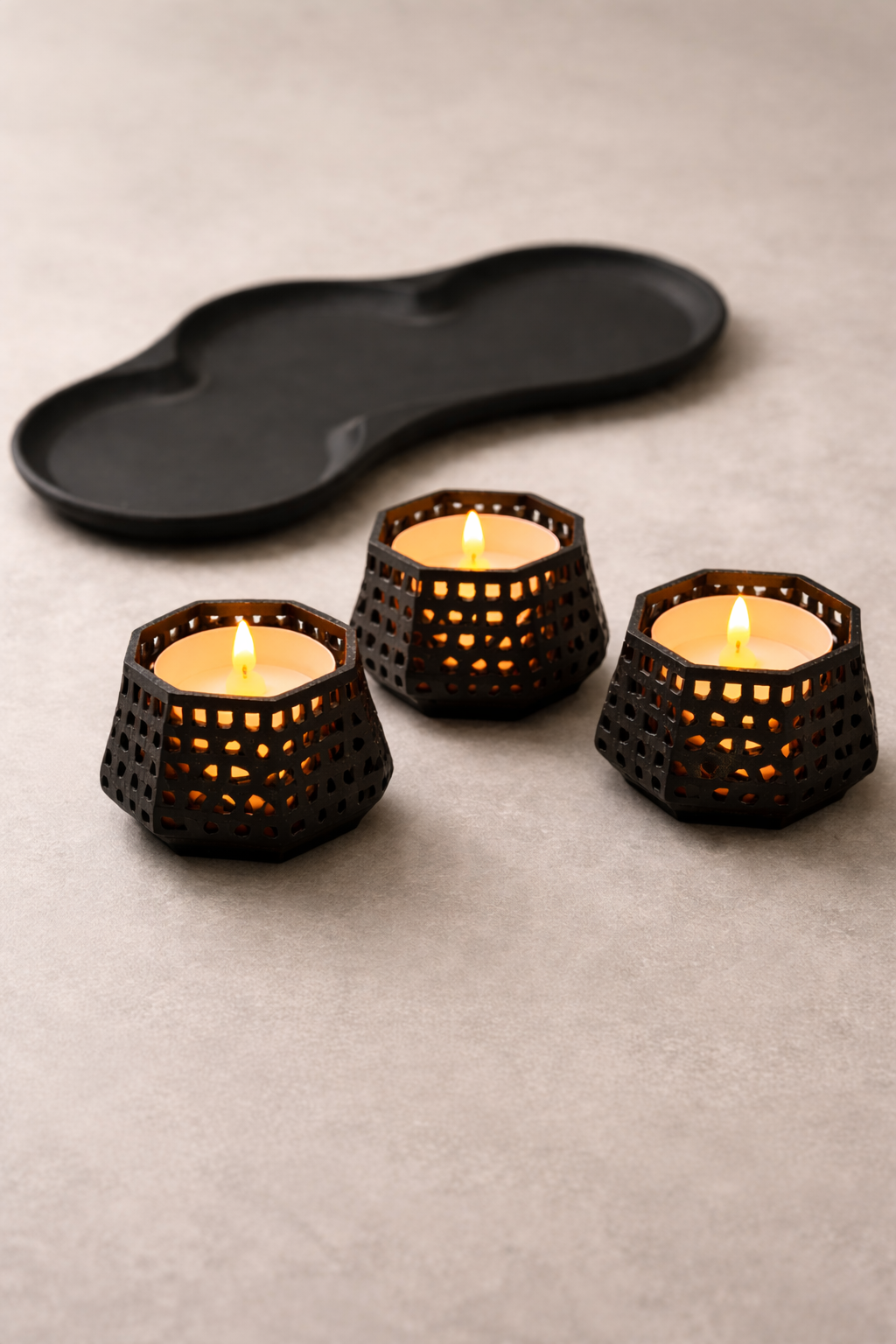 Three lattice tealight holders and tray on a neutral background showing warm candlelight
