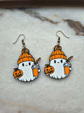 Pair of kawaii ghost Halloween earrings with orange beanie, pumpkin spice latte, and jack-o-lantern on marble surface