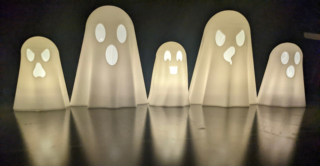 Five glowing 3D printed ghost lanterns with different face expressions lit up in a row on a reflective surface