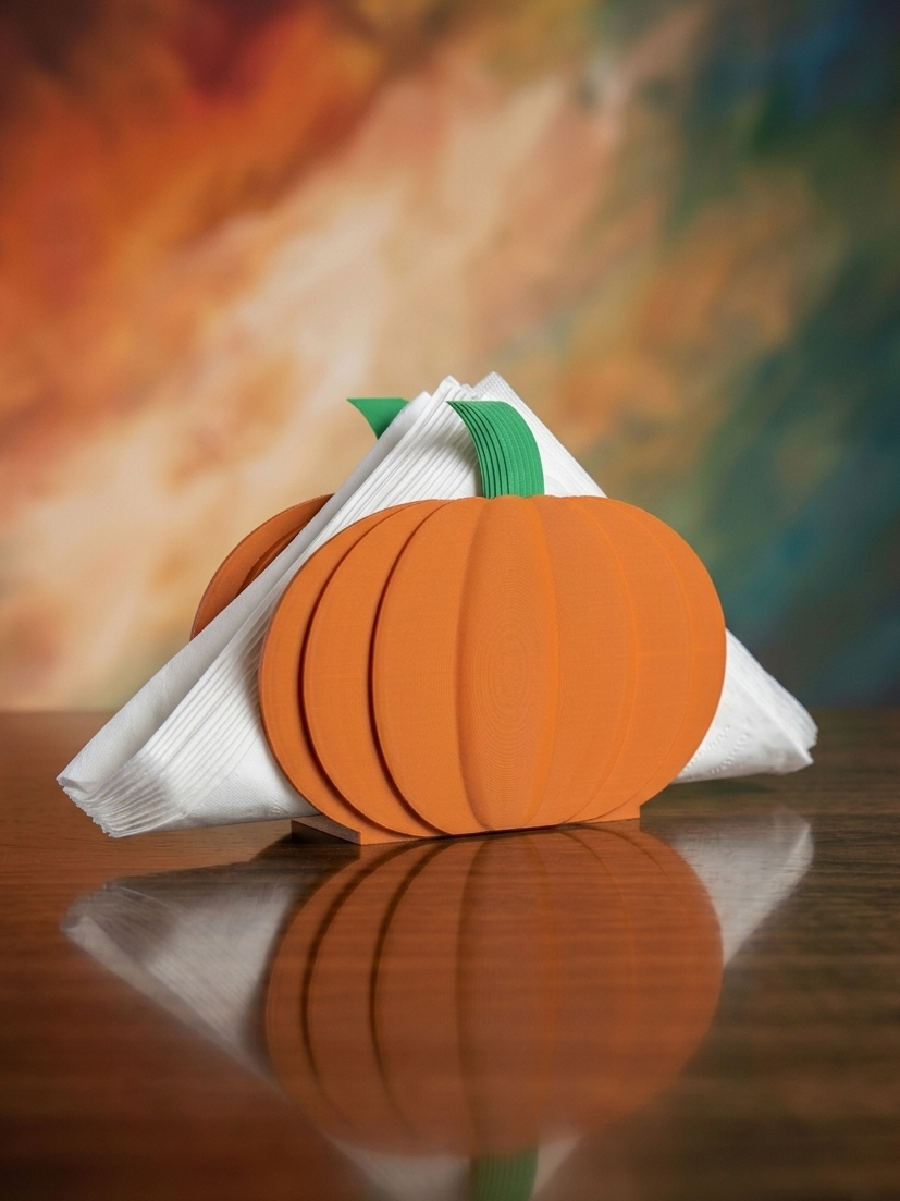 Pumpkin napkin holder holding white napkins with colorful autumn background