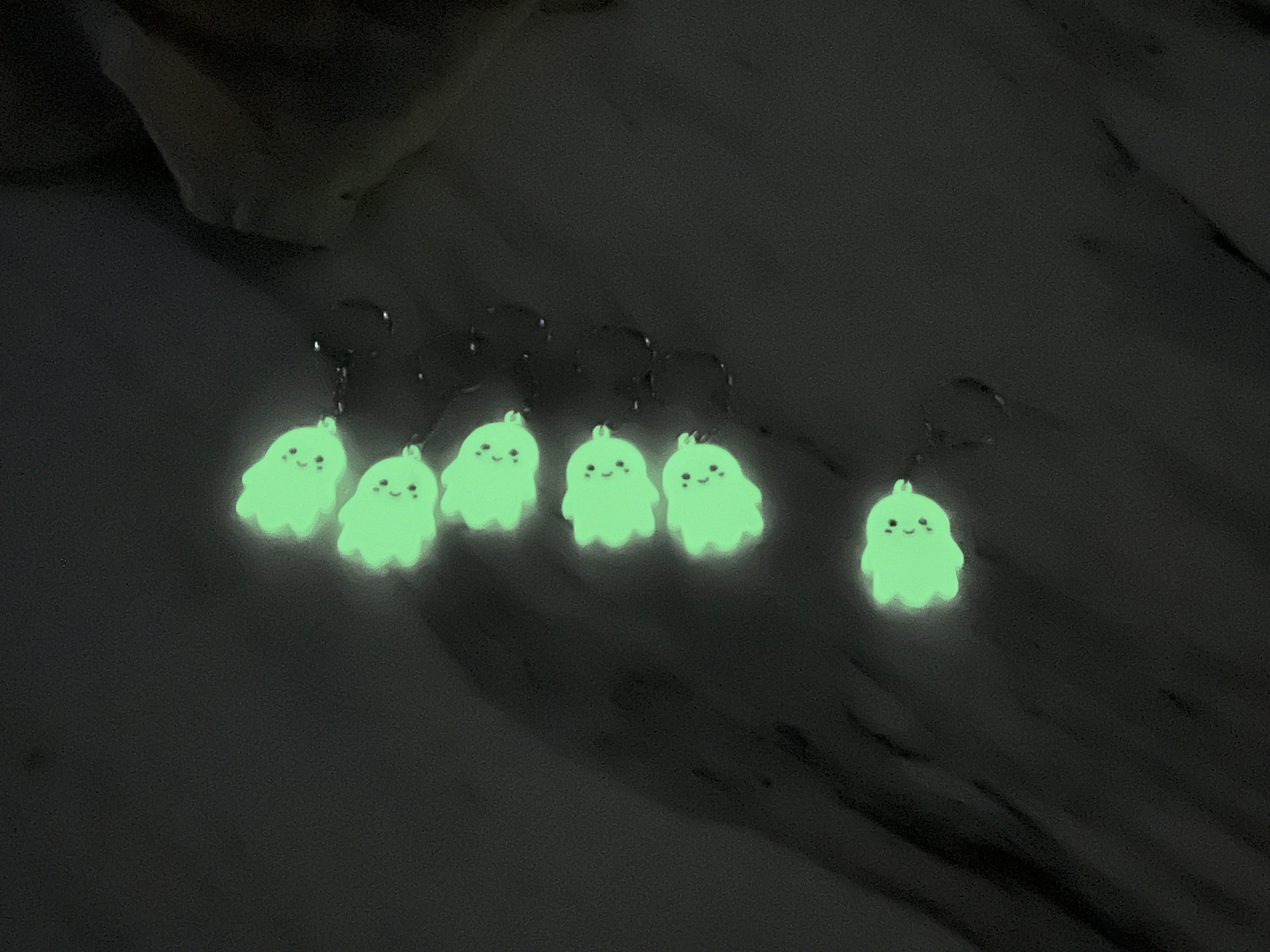 Six glow-in-the-dark ghost keychains glowing bright green in the dark